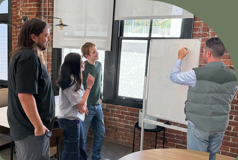 Four Found teammates working through an idea at a whiteboard in a brick-walled room