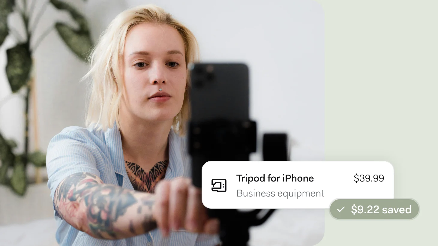 A young blonde woman with tattoos reaches toward the camera while sitting at a desk with a computer monitor in the background. A digital receipt overlay shows "Tripod for iPhone - $39.99" with "$9.22 saved."RetryClaude can make mistakes. Please double-check responses.