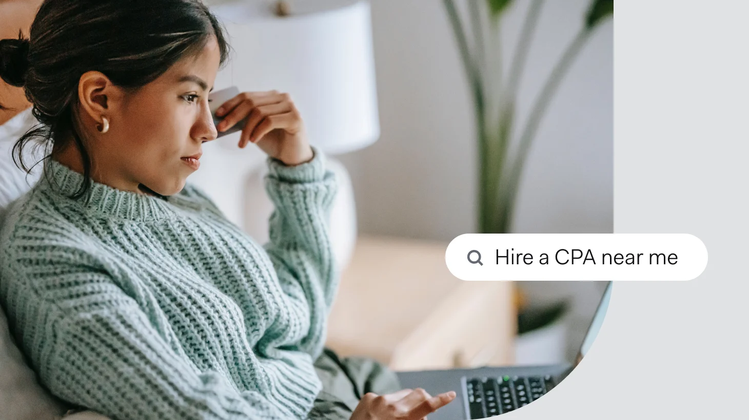 A woman looking stressed at her laptop while holding a card to her temple, beside a search bar reading 'Hire a CPA near me'