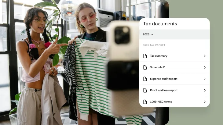 Two young women in a modern office setting are examining clothing items together, with one woman wearing yellow-tinted glasses and holding a green and white striped garment while the other woman, wearing pink-tinted glasses, looks on. In the foreground, there's a white interface panel displaying "Tax documents" with a dropdown menu set to "2025" and a list of tax-related documents including "Tax summary," "Schedule C," "Expense audit report," "Profit and loss report," and "1099-NEC forms" under a "2025 TAX PACKET" heading.