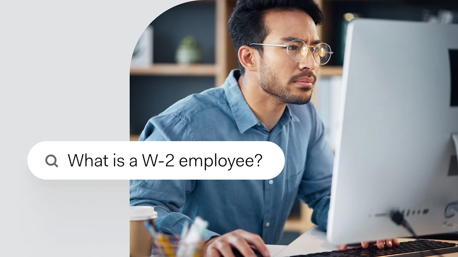 A man working at a desktop computer, with a search bar overlaid showing the typed query 'What is a W-2 employee?'