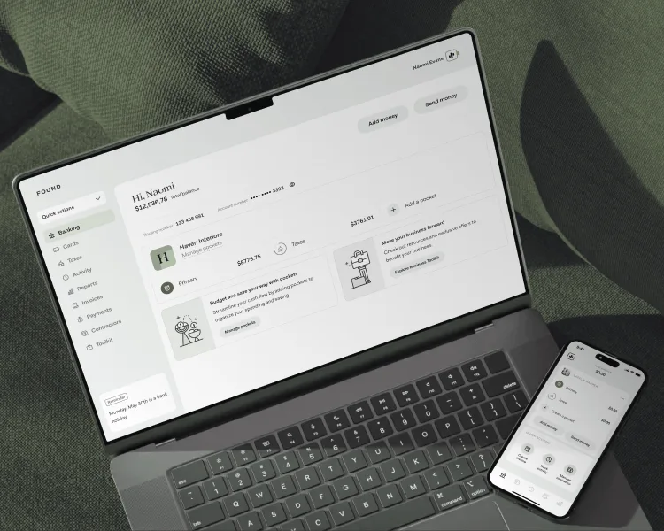 A laptop and phone on a linen chair, both showing the Found app — the laptop on a business account with its balance, pockets and taxes, the phone on the same account's quick actions