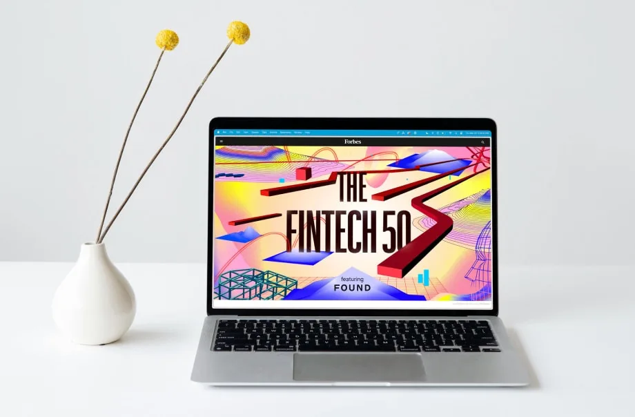 A laptop on a desk beside a vase of dried billy buttons, showing the Forbes Fintech 50 cover featuring Found