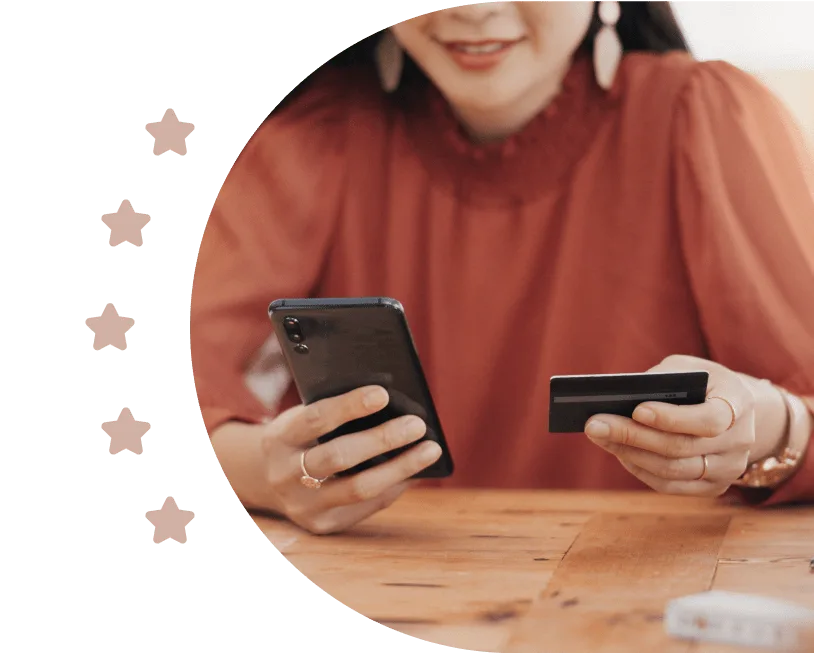 A business owner at a table holding a phone in one hand and a debit card in the other, beside a row of stars